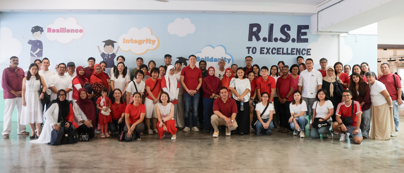 Group of parents and staff posing in front of R.I.S.E to Excellence Wall. Many in red.